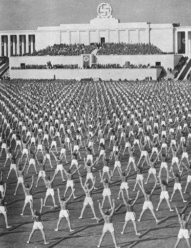 Klassizistisches Gebäude mit Hakenkreuz und vielen Sportlern bei gymnastischen Übungen