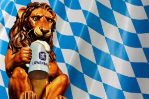Sculpture of a lion with a beer mug in front of the white-blue diamonds of the Bavarian flag